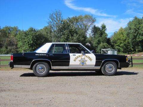 1991 Ford LTD Crown Victoria - Profile of a black-and-white Highway Patrol Ford sedan showing the door shield, front push bar, and roof-mounted antennas.