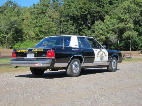 1991 Ford LTD Crown Victoria - Rear three-quarter view of a black-and-white Highway Patrol Ford sedan with yellow HIGHWAY PATROL trunk lettering and roof lights.