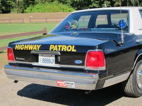1991 Ford LTD Crown Victoria - Close rear view of a black Highway Patrol Ford LTD Crown Victoria with yellow lettering, roof lights, California plate 888849, and an anti-…
