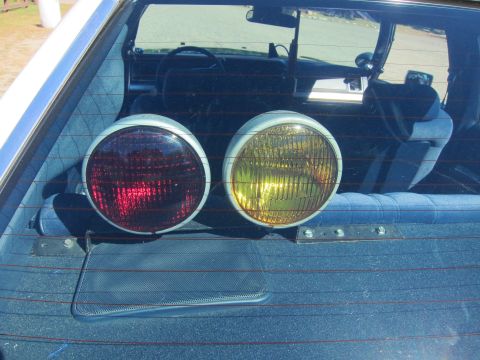 1991 Ford LTD Crown Victoria - pair of round sealed-beam auxiliary lamps, one with a red lens and one amber, mounted on the rear parcel shelf behind the back glass.