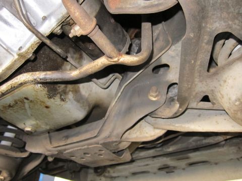 1991 Ford LTD Crown Victoria - Undercarriage view showing a transmission case, exhaust pipe and a stamped-steel crossmember bracket.
