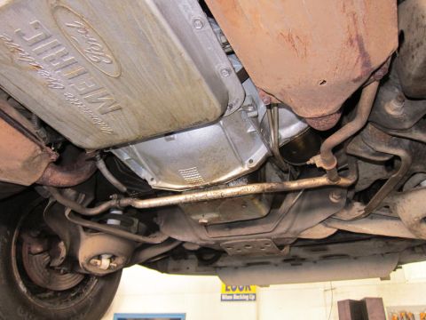 1991 Ford LTD Crown Victoria - Underside view of a transmission pan stamped with the Ford oval and 'Merkur' script, alongside exhaust piping and a tire.