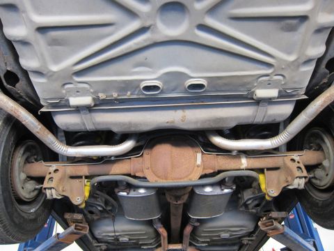 1991 Ford LTD Crown Victoria - Undercarriage view of a solid rear axle flanked by dual exhaust pipes and black air-spring bags on a lift.