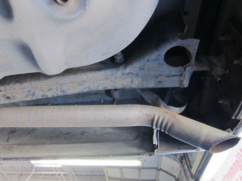 1991 Ford LTD Crown Victoria - Undercarriage view of a rust-coated exhaust pipe with an angle-cut tip routed past a crossmember and oil pan.