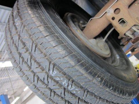 1991 Ford LTD Crown Victoria - Close-up of an all-season tire's tread and a steel wheel on a vehicle raised on a shop lift.