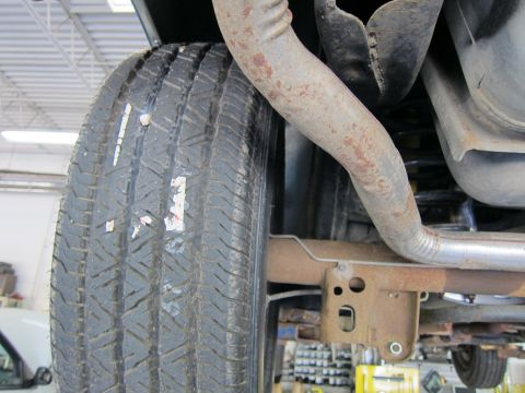 1991 Ford LTD Crown Victoria - View of a tire alongside a rust-streaked exhaust pipe and frame rail in the wheel-well area of a lifted vehicle.