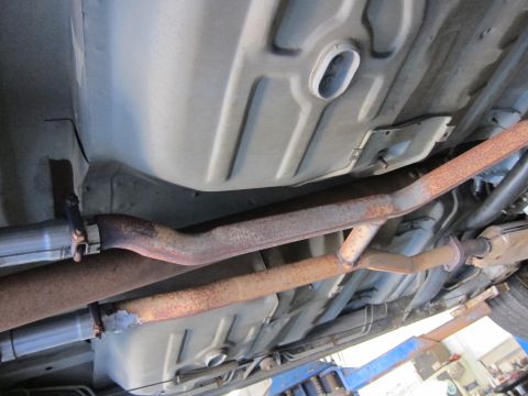 1991 Ford LTD Crown Victoria - Undercarriage view of a fuel tank with two parallel exhaust pipes, one rust-coated, running beneath it.
