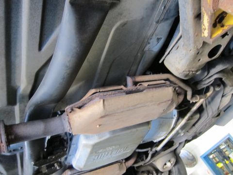 1991 Ford LTD Crown Victoria - Undercarriage view of a transmission pan and tailshaft housing with exhaust and a yellow-tagged component nearby.
