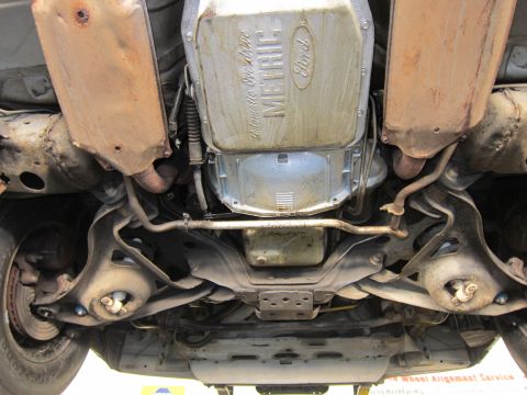 1991 Ford LTD Crown Victoria - Undercarriage view of a Ford-stamped 'Manufactured Metric' transmission pan, crossmember and dual exhaust on a lift.