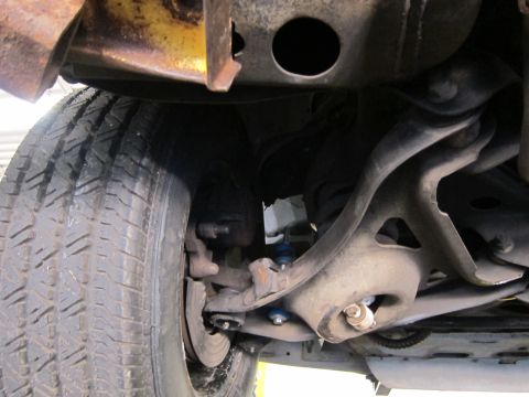 1991 Ford LTD Crown Victoria - Undercarriage view of a front wheel, tie rod and control arm with a blue paint-marked ball joint or fastener.