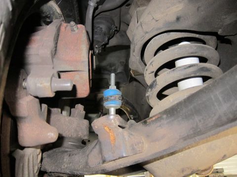 1991 Ford LTD Crown Victoria - Close undercarriage view of a front coil spring, rusty brake caliper and a ball joint stud marked with blue paint.
