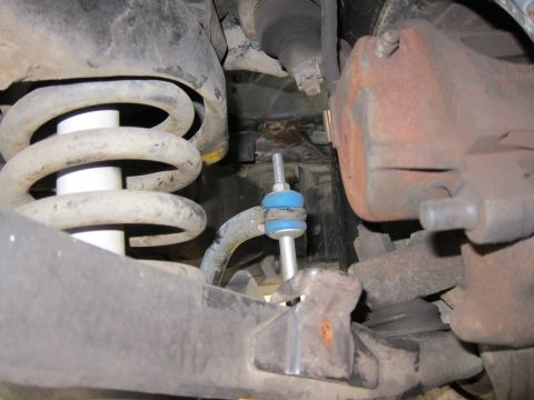 1991 Ford LTD Crown Victoria - Undercarriage view of a front coil spring, rust-coated brake caliper and steering linkage with a blue-marked stud.