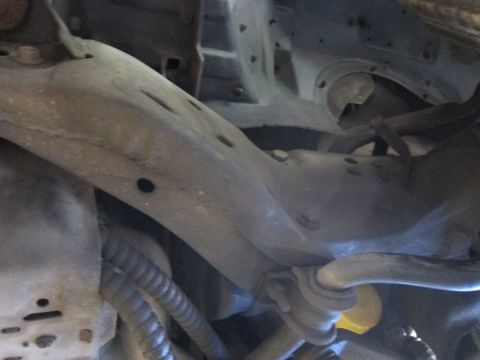 1991 Ford LTD Crown Victoria - Close-up of a vehicle's undercarriage showing the front subframe crossmember, control arm, and surrounding suspension components.