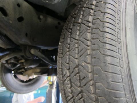 1991 Ford LTD Crown Victoria - Close-up of a tire's tread pattern beside undercarriage suspension components of a raised vehicle.