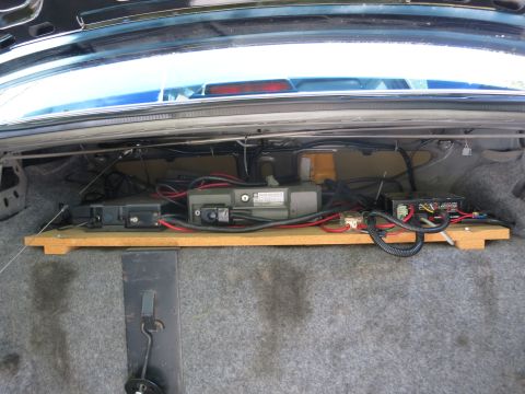 1991 Ford LTD Crown Victoria - Open car trunk showing electronic modules and wiring mounted on a wooden board across the rear shelf area.