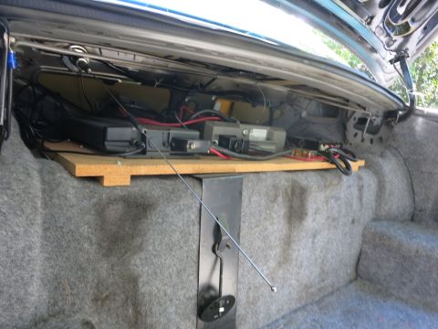 1991 Ford LTD Crown Victoria - Open trunk showing mounted electronics on a wooden board with a thin antenna mast extending across the carpeted floor.