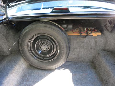 1991 Ford LTD Crown Victoria - Open car trunk showing a black steel spare wheel and tire beside electronics mounted on a wooden board.