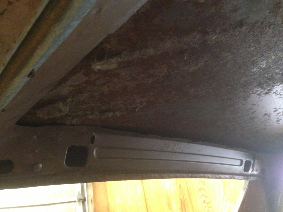 Rusted interior ceiling of a vehicle, showing structural beams and insulation