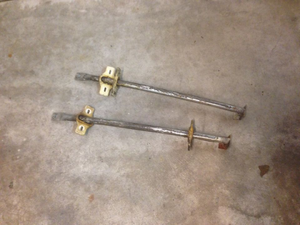 Two metal rods with mounting brackets on a concrete floor