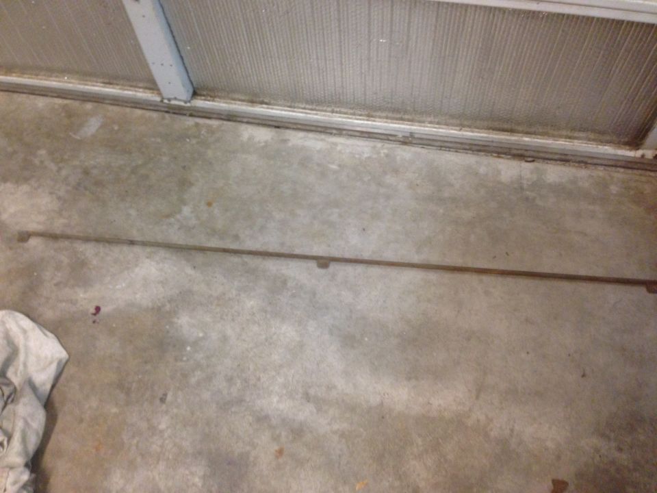 Long, thin metal trim piece with two small brackets, lying on a concrete floor