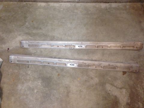 1972 Ford Ranchero - Two aluminum running boards, each a Ford emblem and a series of rectangular cutouts, lie on a concrete floor.