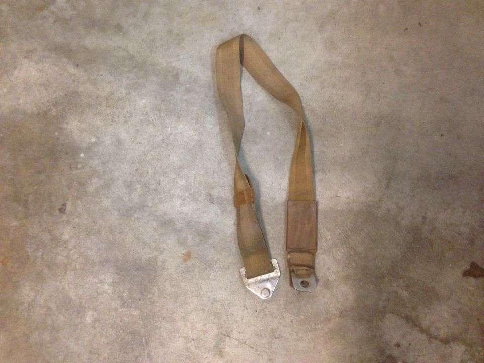 Tan seatbelt with metal buckle and anchor points on a concrete floor