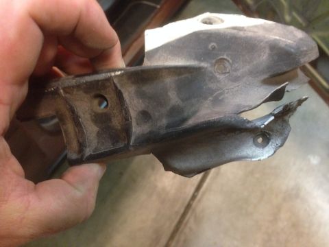 1972 Ford Ranchero - A damaged metal bracket is held in a hand, showing its mounting holes and bent edges.