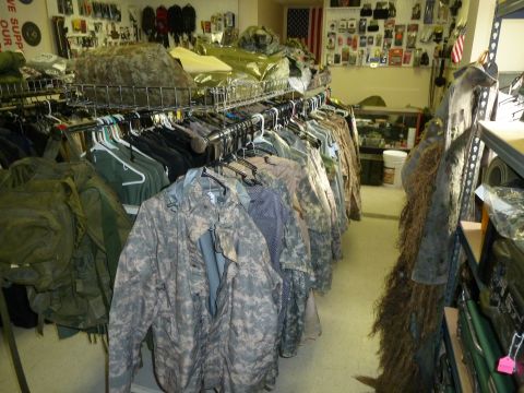 1992 Ford Mustang - A store interior displays various military-style clothing and gear on racks, with shelves stocked in the background.