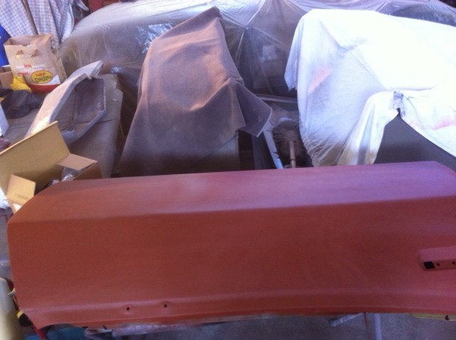 red car door in foreground, other vehicles covered in tarps behind it