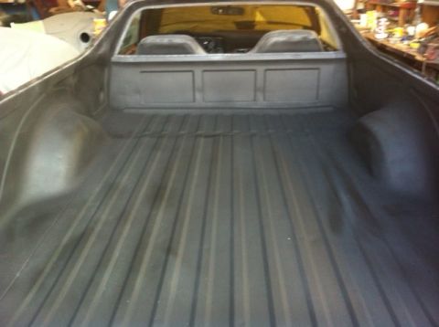 1972 Ford Ranchero - The bed of a 1972 Ford Ranchero shows a dark gray, ribbed surface with a visible interior and rear window.