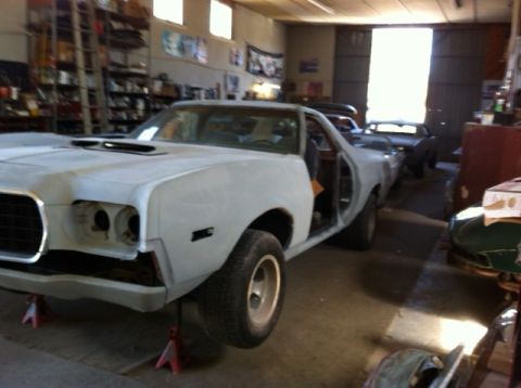 1972 Ford Ranchero - A light-colored car in a garage, with its front end missing parts and doors open, sits on red jack stands.