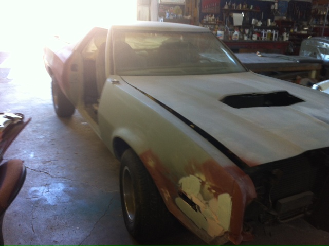 car body with primer and bondo, hood scoop, doors open, in a workshop