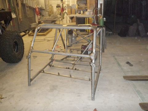 1961 International Scout 800 - A custom-fabricated roll cage structure is shown in a workshop setting, with a large tire nearby.