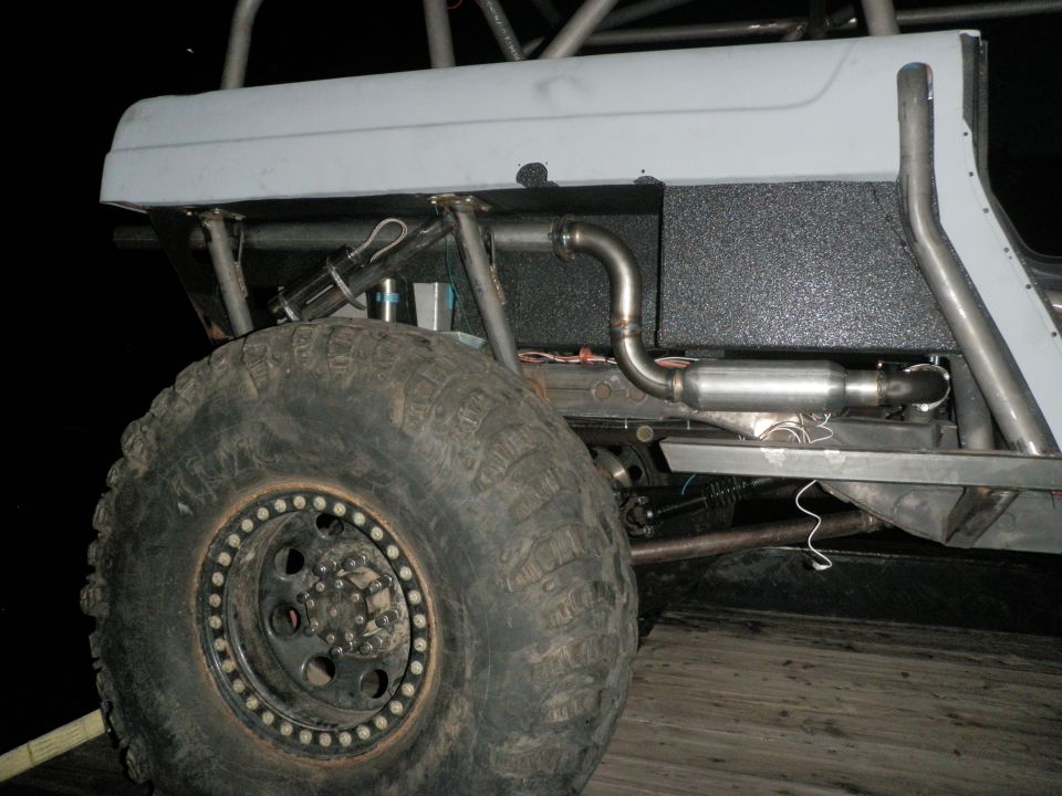 Close-up of custom exhaust pipe and muffler on a modified off-road vehicle, showing a large tire and roll cage