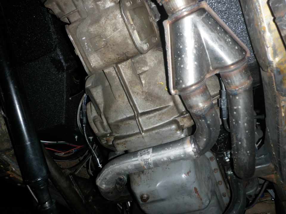 Close-up of a Y-pipe exhaust collector and transmission housing, with visible wiring and oil pan