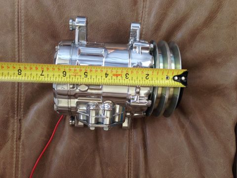1964 Ford Fairlane - A chrome AC compressor is measured with a tape measure against a brown leather background.
