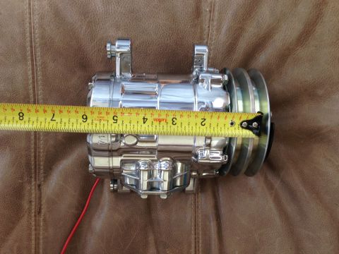 1964 Ford Fairlane - A chrome air conditioning compressor is measured with a yellow tape measure, resting on a brown textured surface.