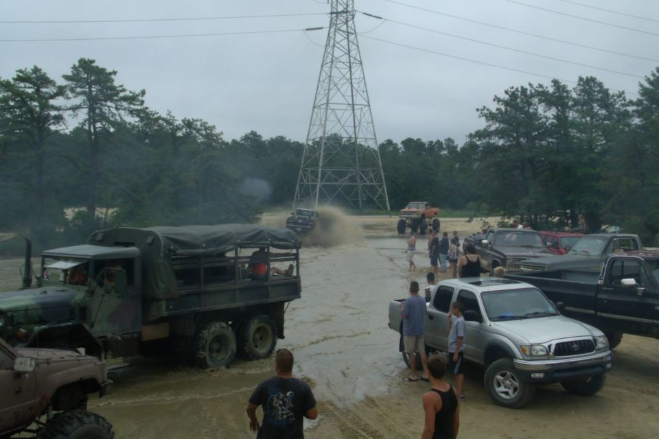 Military truck with canvas cover, parked in mud near other trucks and people