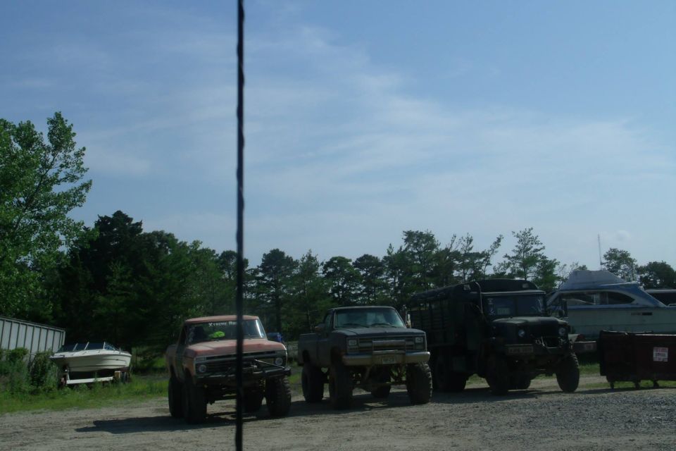 Three lifted trucks parked in a lot. One is orange, one is gray, and the third is a dark green military-style truck