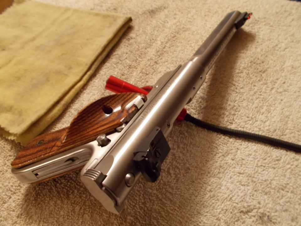 Silver firearm part with wooden grip on a textured surface