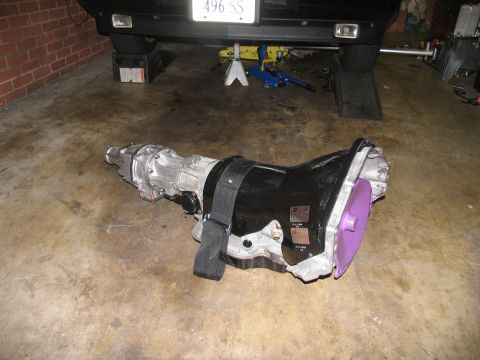 1990 Chevrolet Silverado 1500 - A transmission is shown on a concrete floor, with a vehicle partially visible in the background.