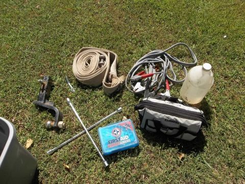 1995 Ford Bronco - Various vehicle accessories including a recovery strap, jumper cables, and a first aid kit are laid out on a grassy surface.