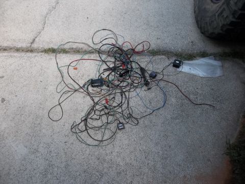 1995 Ford Bronco - A pile of tangled wires and electronic components lies on a concrete surface, with a portion of a vehicle tire visible in the upper right c…