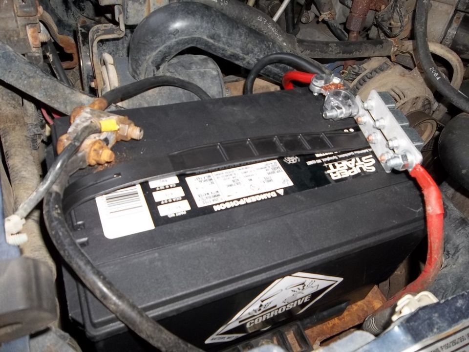 vehicle battery with corroded terminals and engine bay wiring