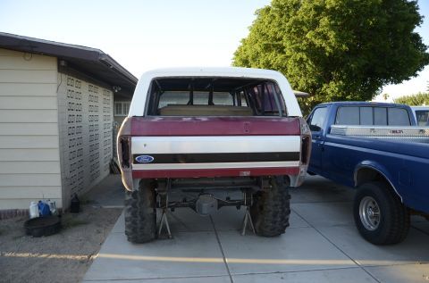1979 Ford Bronco - The rear of a Ford Bronco is shown on jack stands, with a blue pickup truck parked beside it.