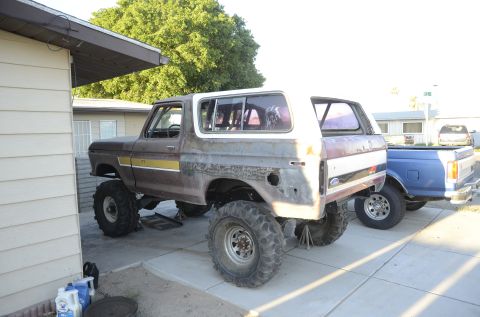 1979 Ford Bronco - A modified 1978 Ford Bronco sits in a driveway next to a blue pickup truck, showing significant bodywork and off-road modifications.