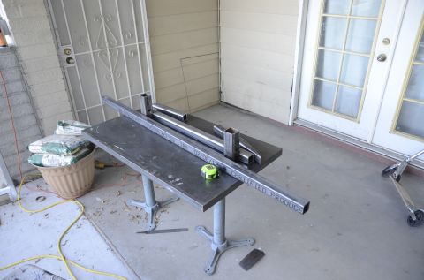 1979 Ford Bronco - Metal tubing is laid out on a workbench, with a tape measure and bags of cement nearby.