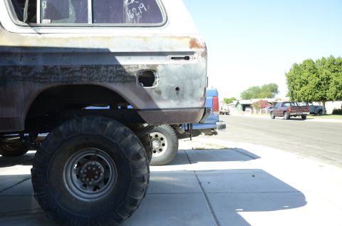 1979 Ford Bronco - A weathered 1978 Ford Bronco is seen from the rear quarter, with other vehicles and houses in the background.