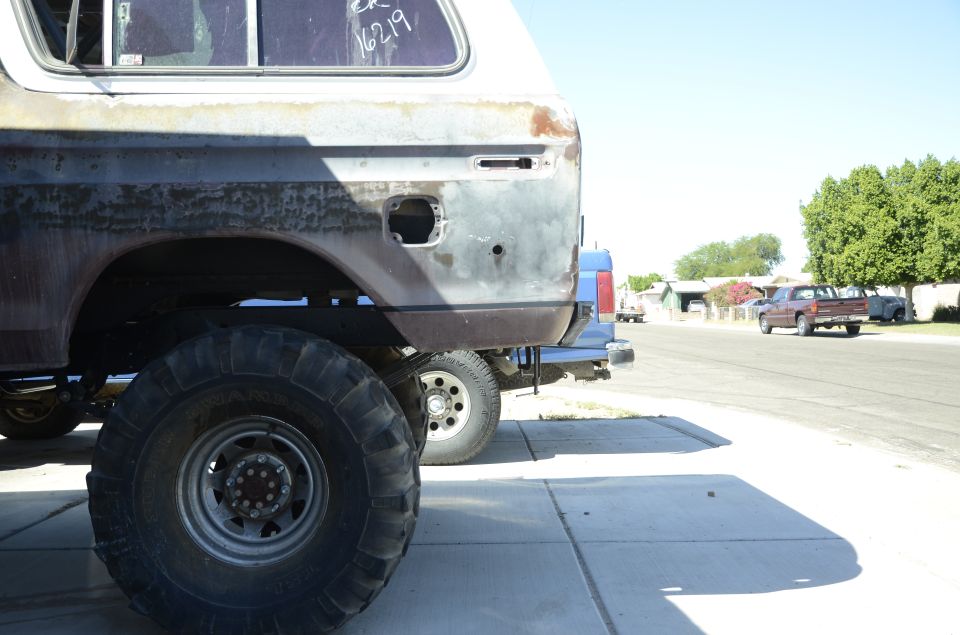 Rear quarter of a rusty 1978 Ford Bronco with large tires, parked next to another vehicle