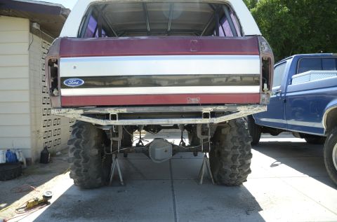 1979 Ford Bronco - The rear of a 1979 Ford Bronco is shown on jack stands, with a blue pickup truck visible to the right.